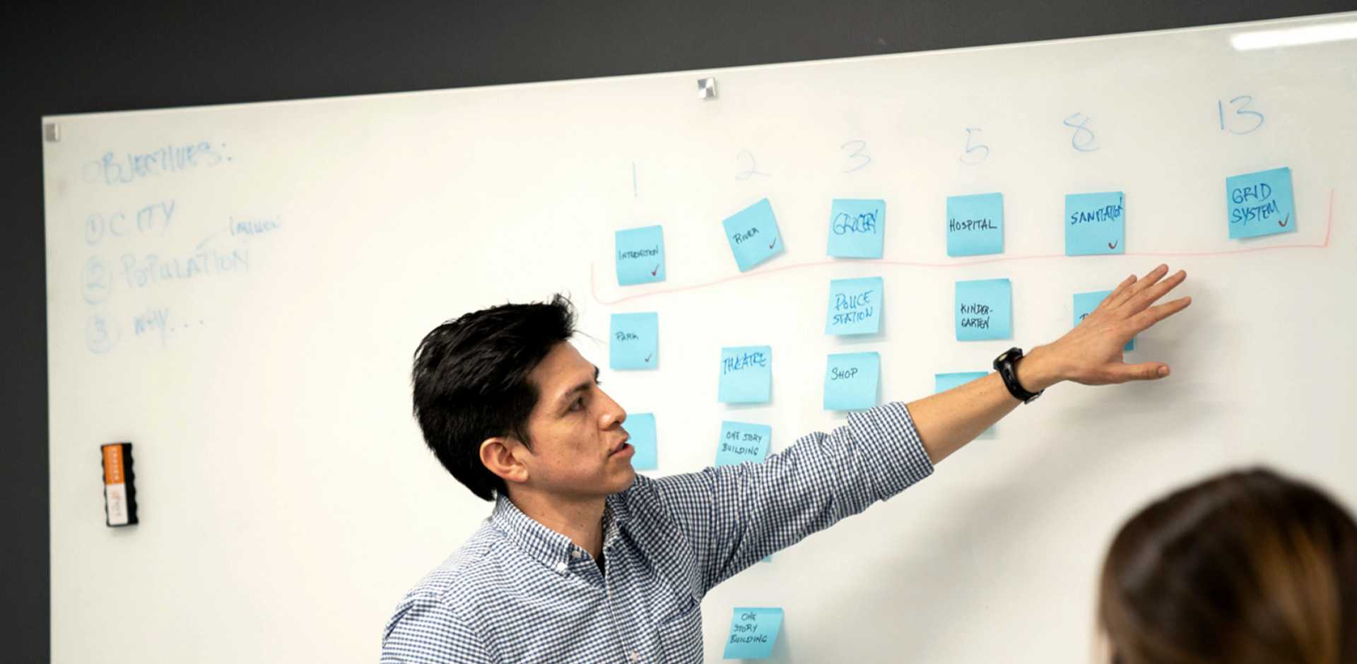 A man pointing to sticky notes on a white board.