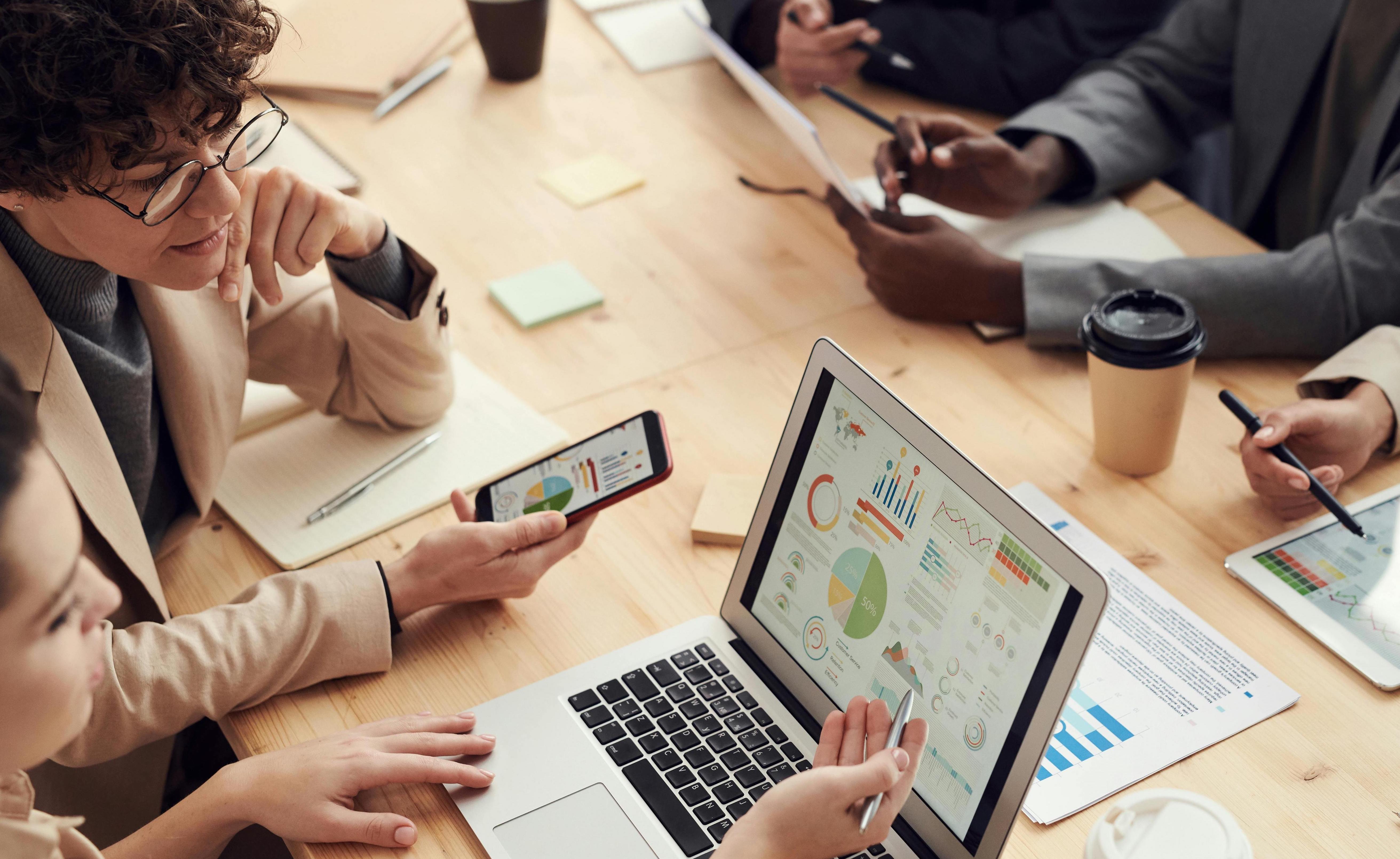 Diverse team collaborating in an office setting using laptops and tablets improving customer experience through cross-functional teamwork. Photo by Fauxels via Pexels.