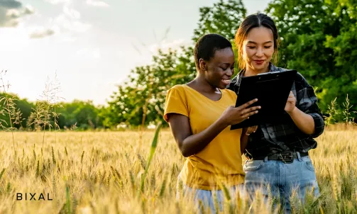 Two women stand in a field of tall grass looking at a tablet.