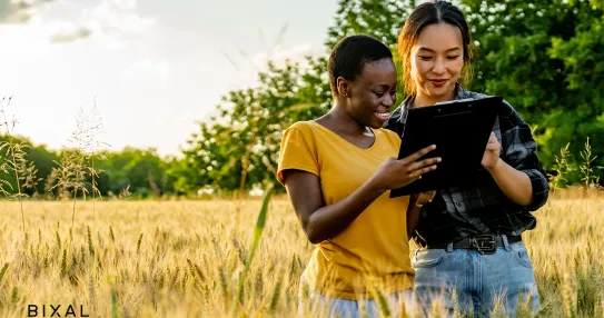 Two women stand in a field of tall grass looking at a tablet.