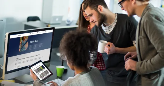 A group of people stand around a table looking at a computer screen.