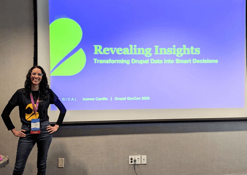 Bixaler Ivonne Carillo, a woman with long dark hair and glasses, stands in front of a screen upon which is projected the title slide of her Drupal GovCon presentation, “Revealing Insights: Transforming Drupal Data Into Smart Decisions.