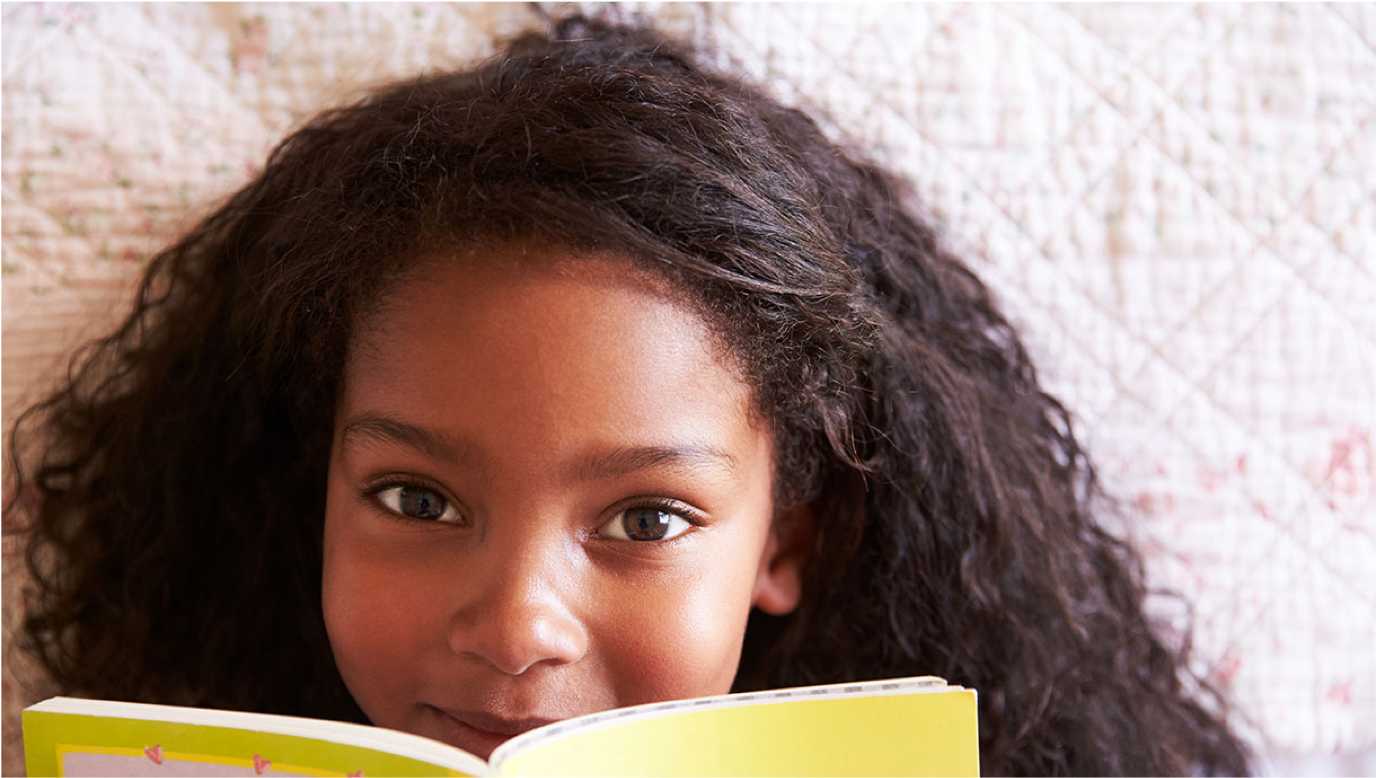 young girl smiling over the edge of a book.