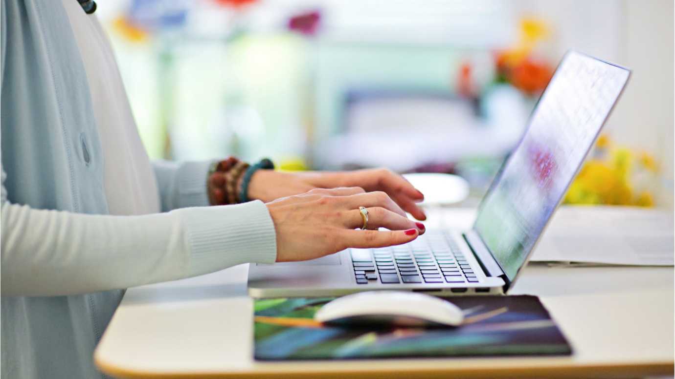 Side view of a woman's hands on the keyboard of a laptop.