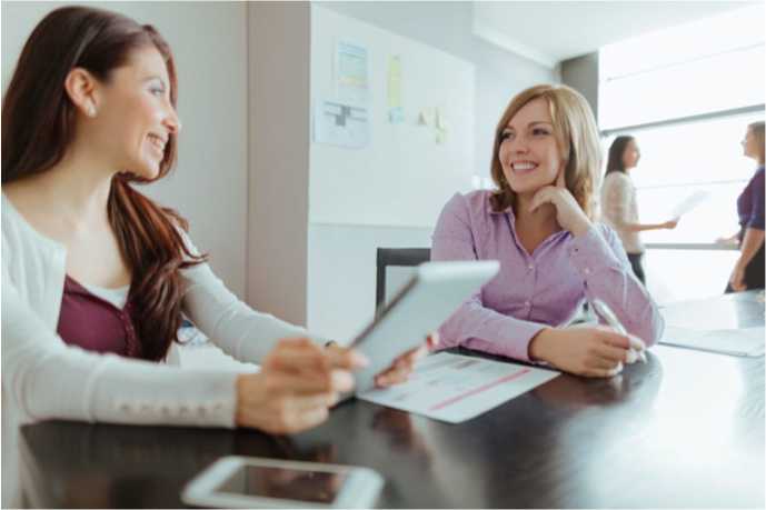 two working women sitting at a conference table conversing